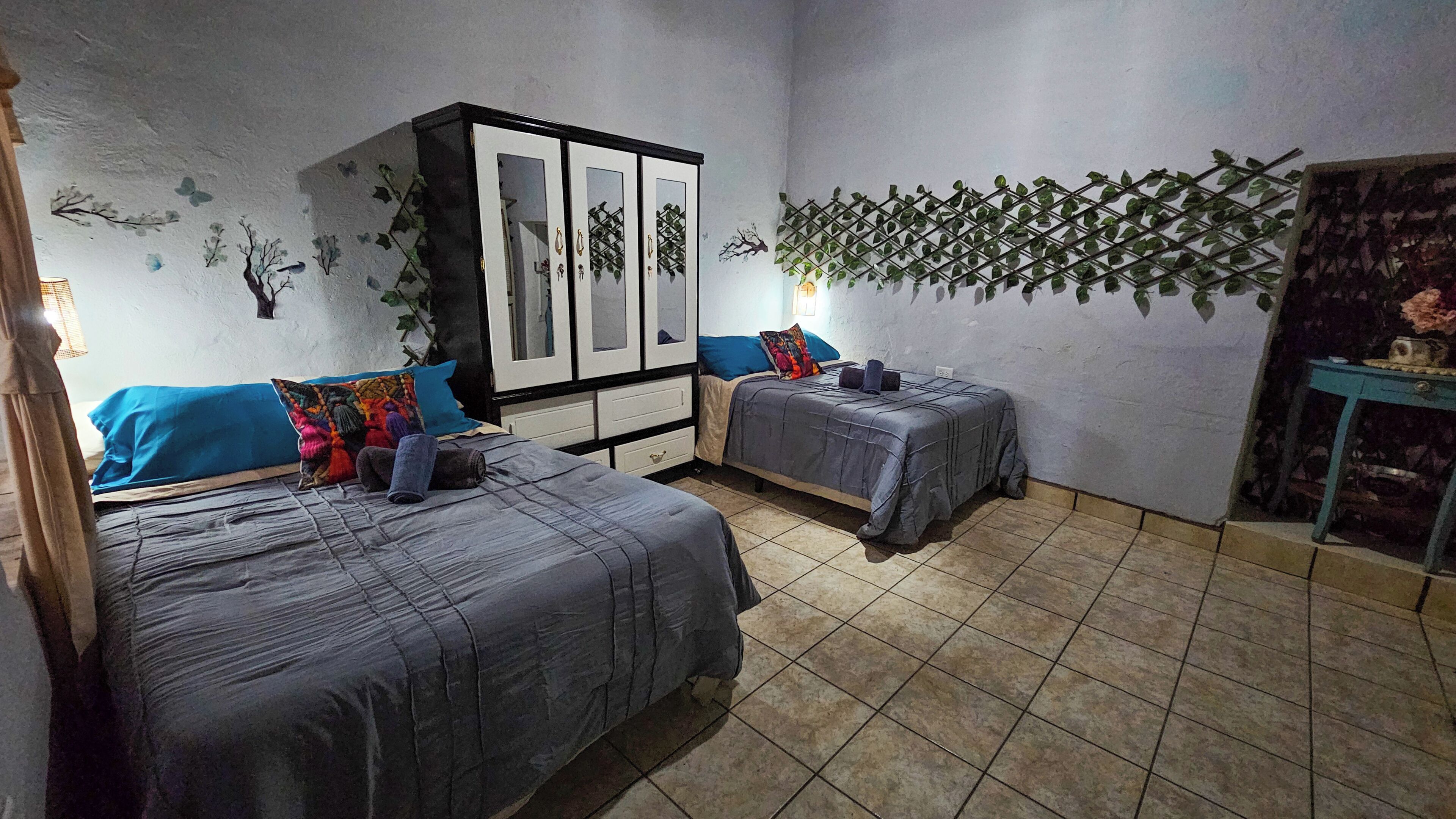 Un dormitorio con dos camas, un armario y una pared decorativa con plantas.