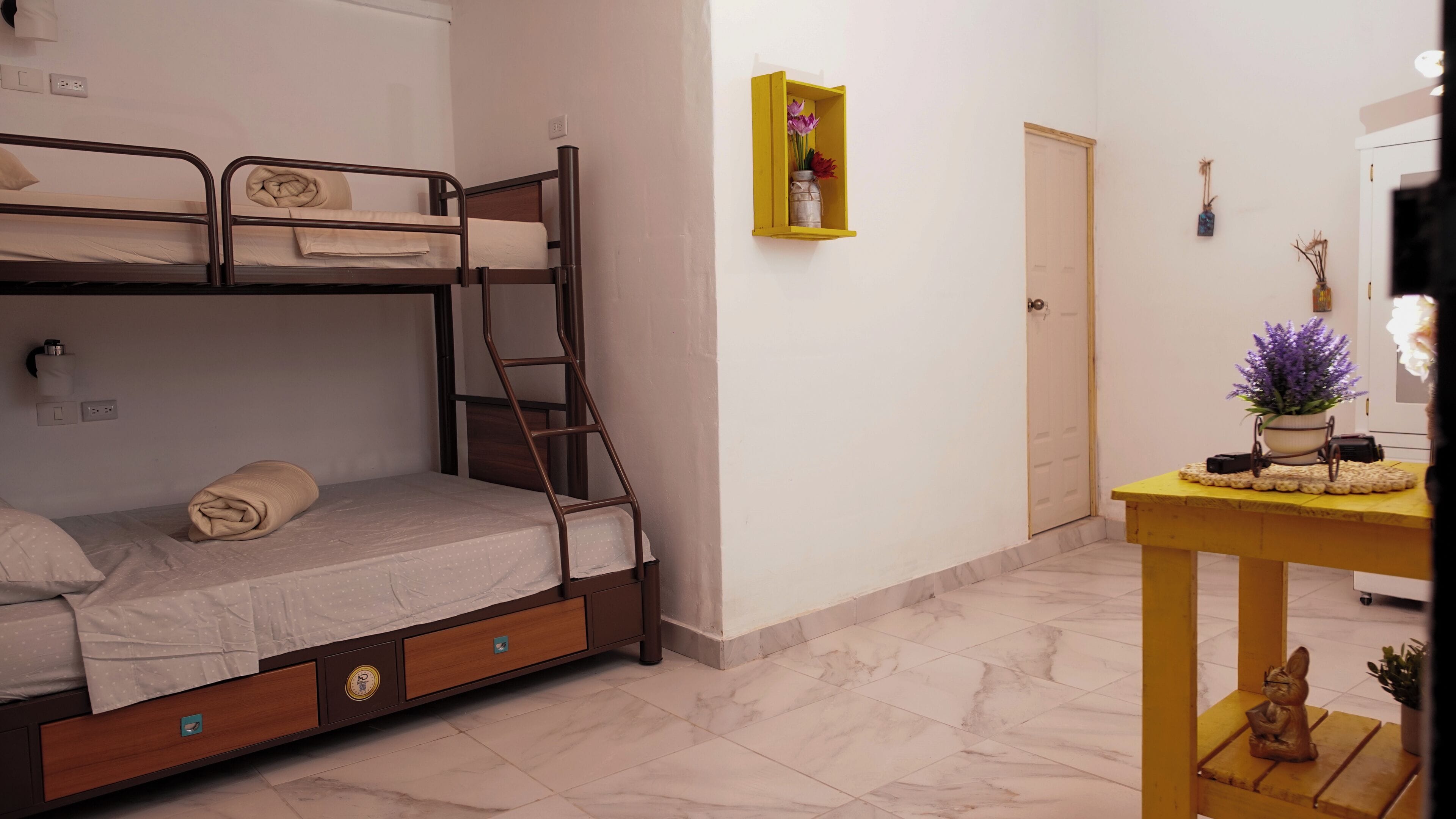 A bedroom with a bunk bed, a small table with a vase, and a door.
