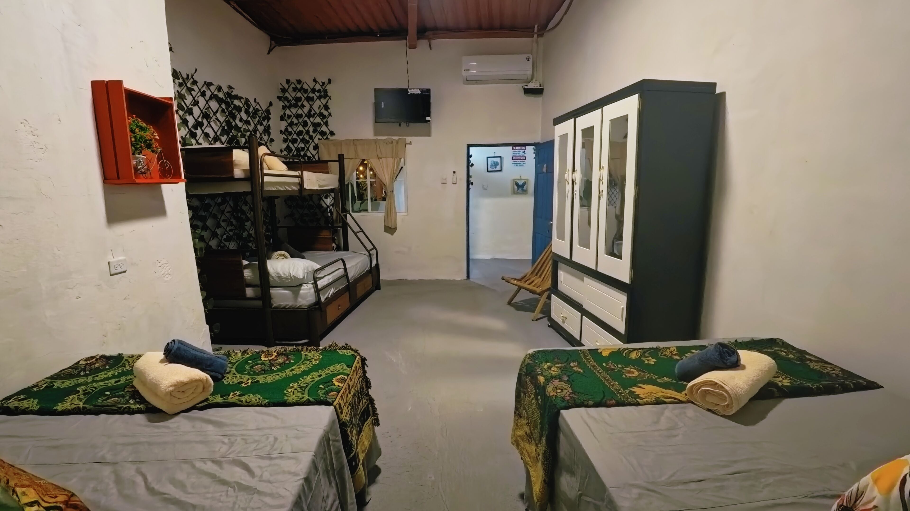 Una habitación con literas, un armario, un televisor y una puerta que da a otra habitación.