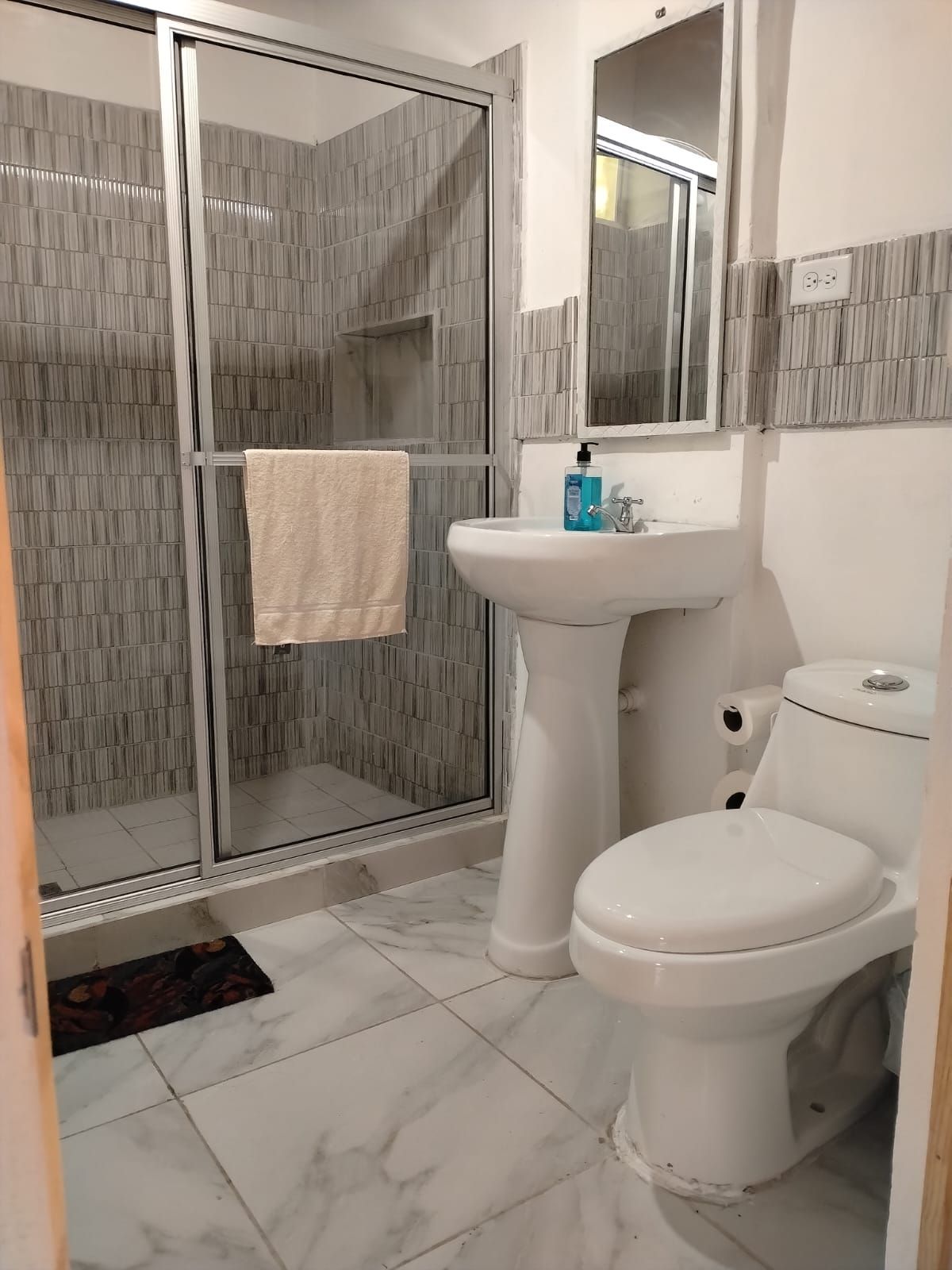 A bathroom with a glass shower enclosure, a white sink, and a toilet.