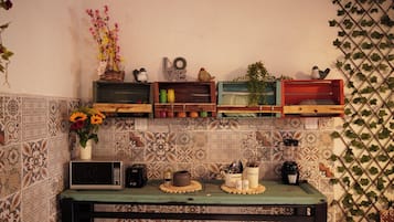 Una cocina con microondas, cafetera y estante con diversos objetos, incluyendo un jarrón con flores.