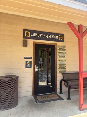 A door labeled 'Laundry / Restroom' with a no smoking and no pets allowed sign, a welcome mat, and a trash can. - Steampunk Tiny House w/ Loft Near Lake Travis (Austin)