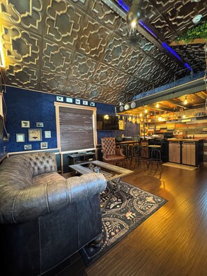 Een modern interieur met een bank, een kamerbreed tapijt met een patroon, een keukenhoek, en een plafond met geometrische motieven.