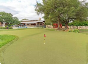 A golf course with a flagstick on the green, a building in the background, and trees around the perimeter. - Steampunk Tiny House w/ Loft Near Lake Travis (Austin)