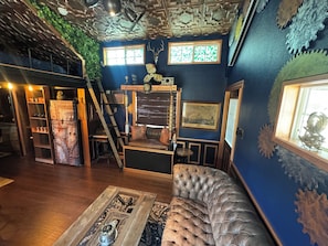 A room with a blue wall, a wooden staircase, a tufted leather sofa, and a decorative ceiling. - Steampunk Tiny House w/ Loft Near Lake Travis (Austin)