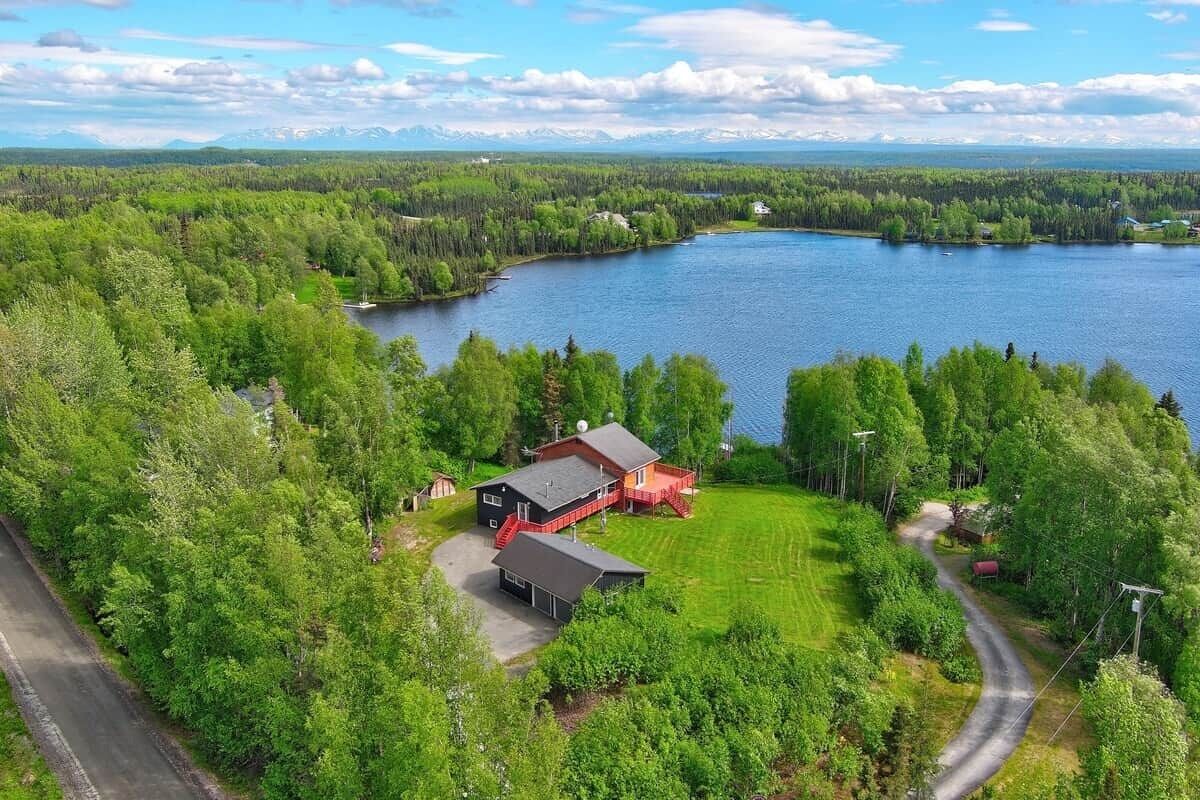 Une propriété située au bord d’un lac, comprenant une maison principale, un garage et un bâtiment dont le toit est rouge.