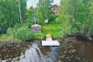A riverside property with a wooden dock leading to a small house, surrounded by dense greenery and trees.