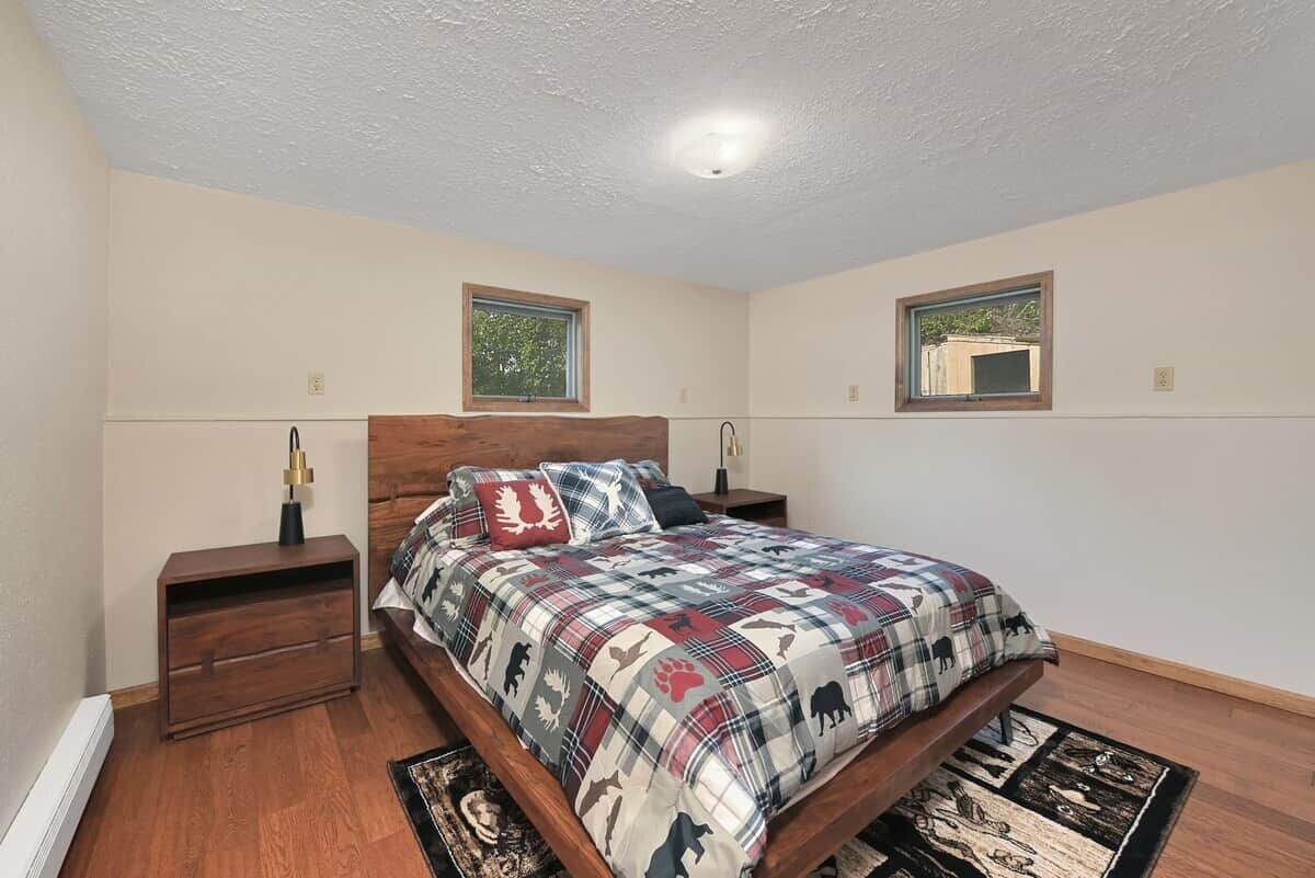 Une chambre à coucher avec un lit en bois, deux tables de chevet, une fenêtre et un luminaire au plafond.