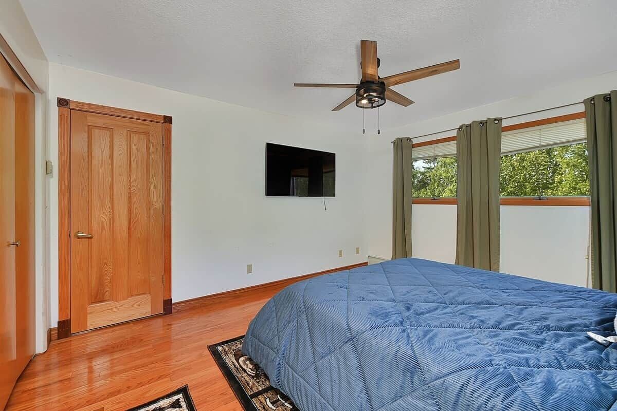 A bedroom with a bed, a ceiling fan, a window with curtains, and a door.