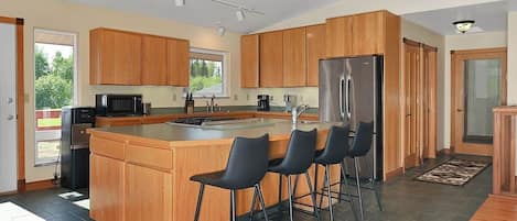 A modern kitchen with wooden cabinets, a stainless steel refrigerator, and a bar area with stools.