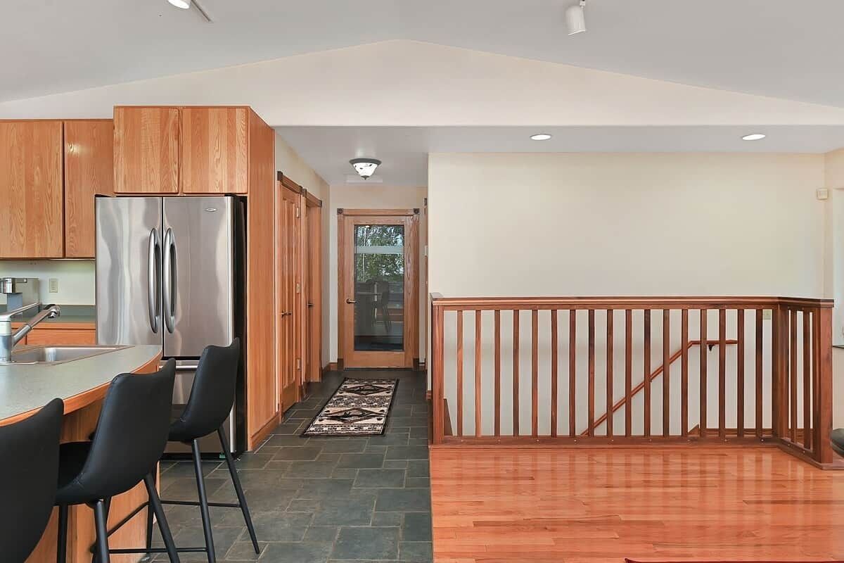 A modern kitchen with a stainless steel refrigerator, wooden cabinets, and a bar area with two black chairs.