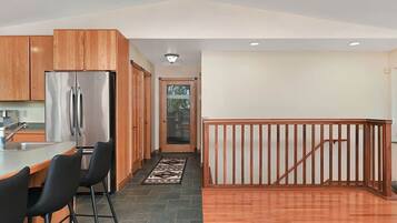 A modern kitchen with a stainless steel refrigerator, wooden cabinets, and a bar area with two black chairs.