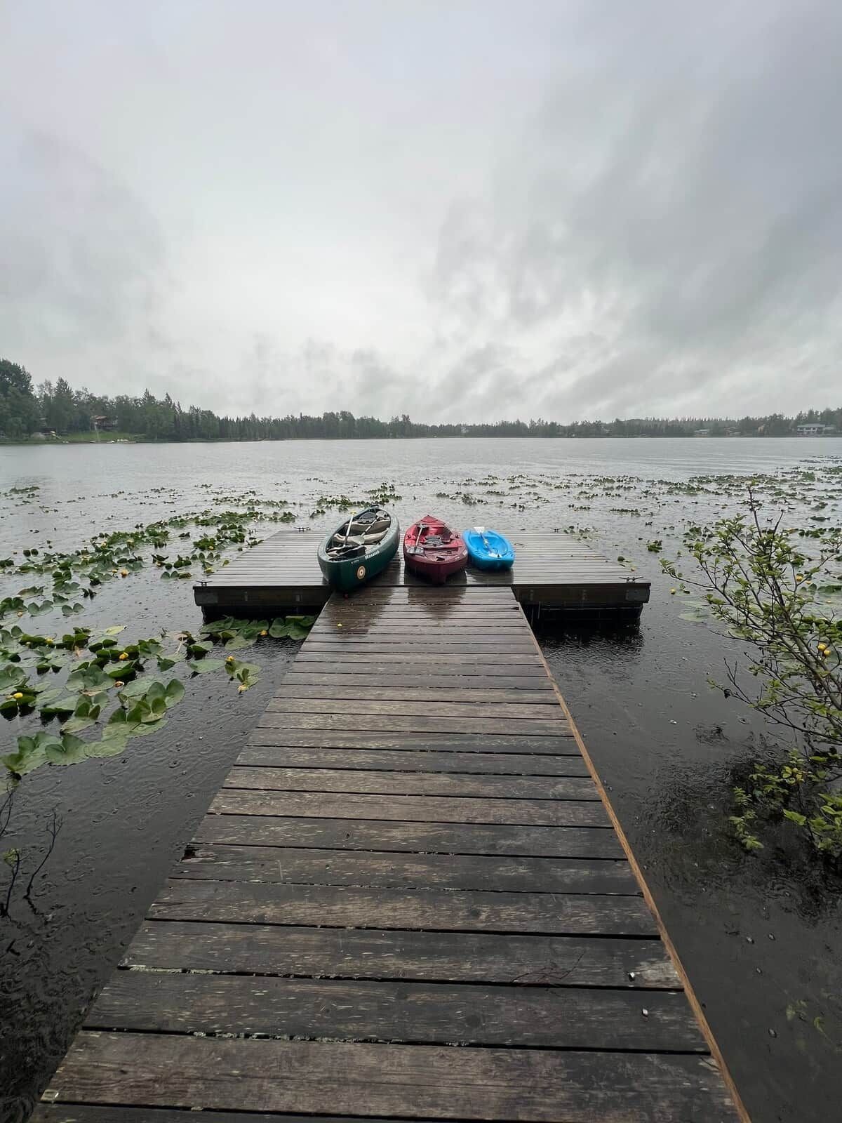 Un muelle de madera que conduce a un lago tranquilo, con tres kayaks amarrados al final.