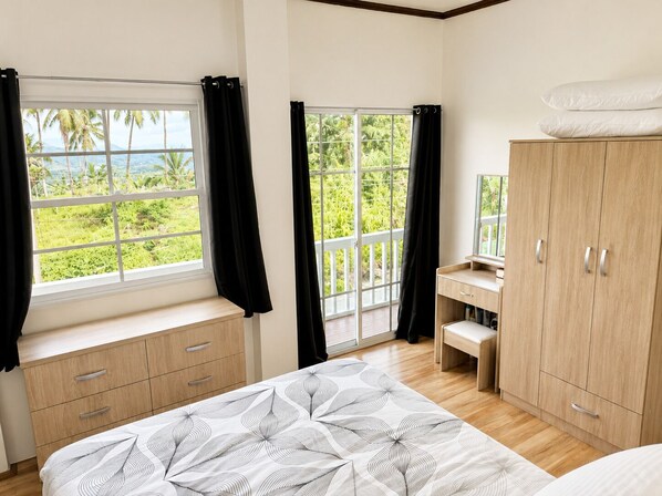 A bedroom with a bed, a desk, a wardrobe, and a window with a view of greenery.
