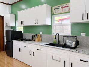 A kitchen with white cabinets, a black refrigerator, a sink with a black faucet, and a window with a view of greenery.