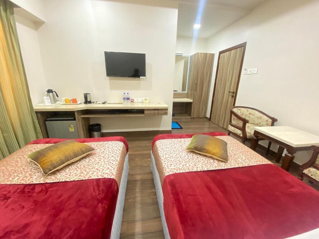A hotel room with two beds, a desk, a chair, a TV, and a bathroom in the background.