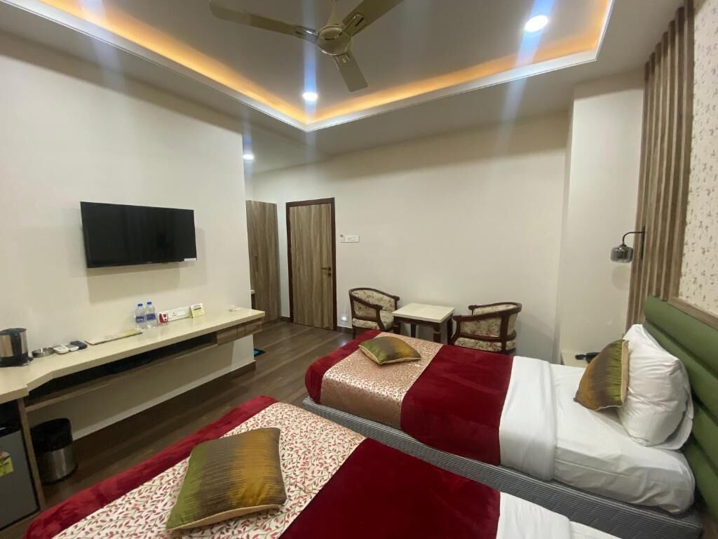 A hotel room with two beds, a desk, a television, and a ceiling fan.