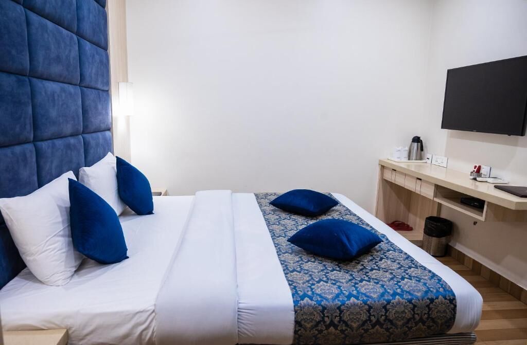 A hotel room with a bed, a flat-screen TV, a desk, and a trash can.