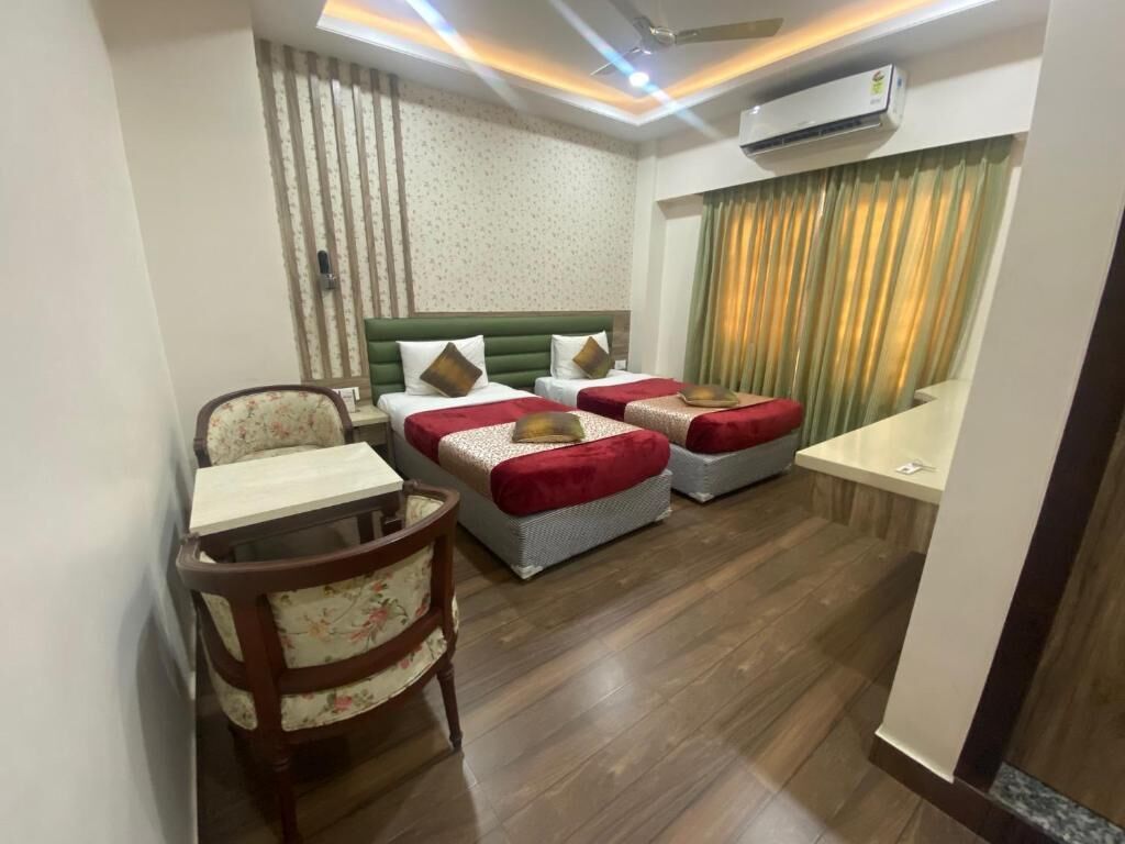 A hotel room with a bed, a chair, a small table, and a window with curtains.