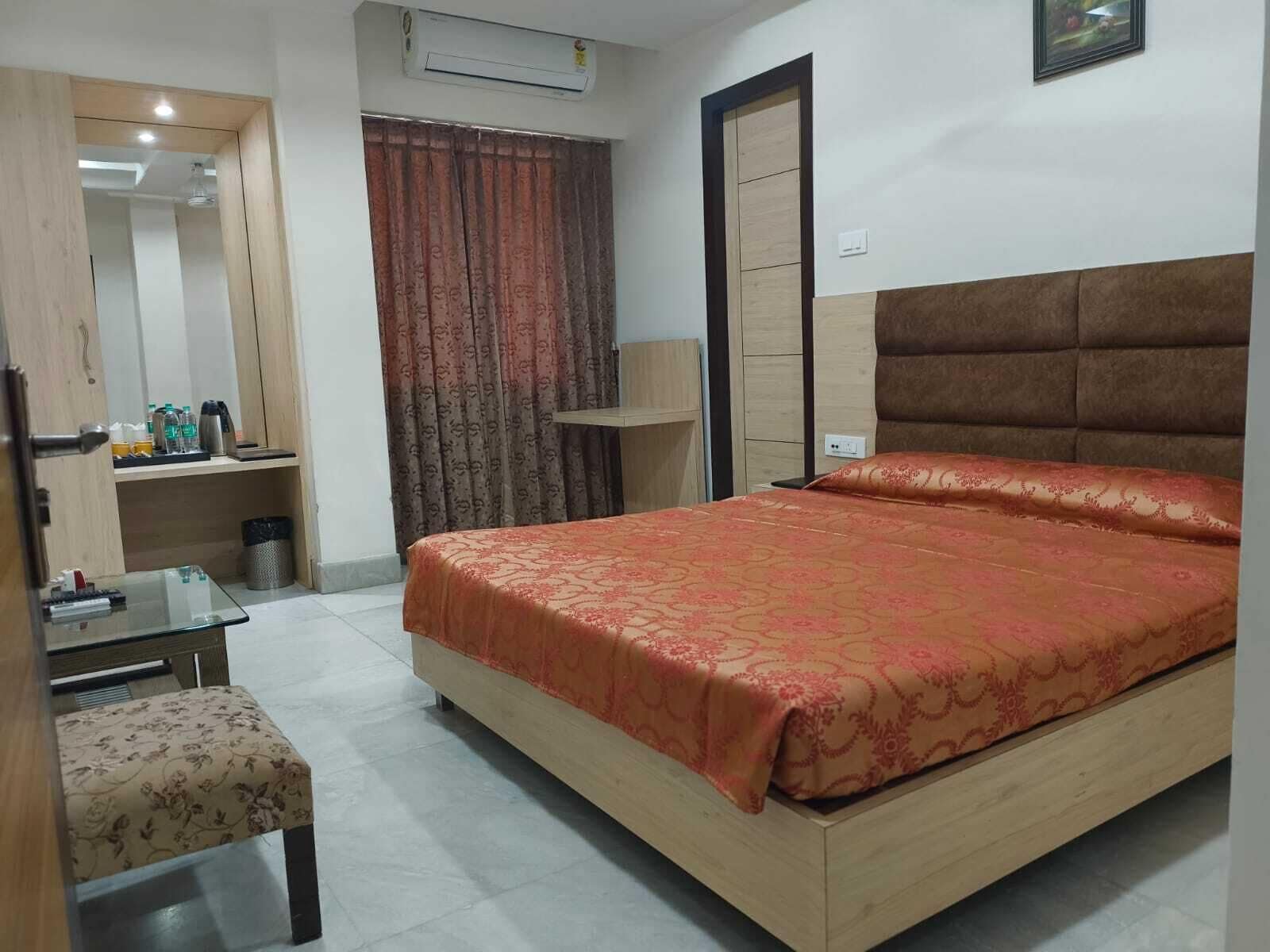 A hotel room with a bed, a desk, a chair, an air conditioning unit, a wardrobe, and a curtain.