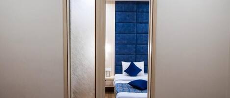 A narrow hallway leading to a bedroom with a tufted headboard and a bed with blue bedding.
