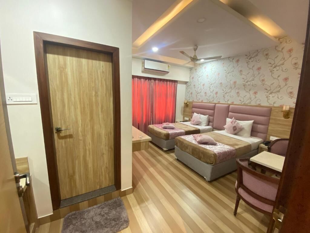 A bedroom with a wooden door, two beds with pink headboards, a ceiling fan, and a patterned wallpaper.