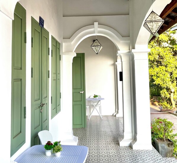 A covered outdoor area with a table and chairs, a potted plant, and a tiled floor.