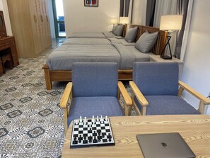 Quarto de hotel com duas camas, uma mesa com um laptop, um tabuleiro de xadrez e uma cadeira.