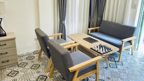 A room with a chessboard on a wooden table, grey sofas, and patterned floor tiles. - La Petite Maison Luang Prabang (Luang Prabang)