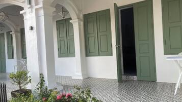 Un edificio con puertas verdes y paredes blancas, piso de baldosas y un pequeño jardín con flores.