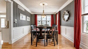 A dining room with a wooden table and chairs, a chandelier, and red curtains.