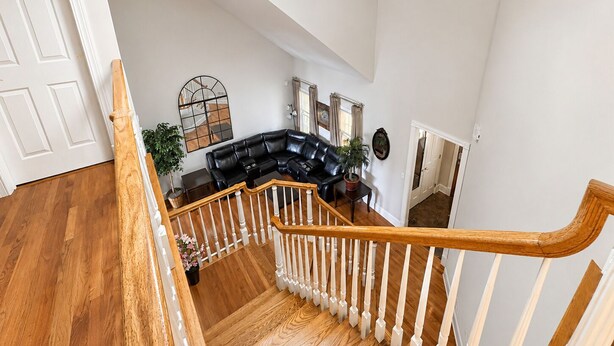 A spacious living area with a black leather sectional sofa, a wooden staircase with white balusters, and a large mirror on the wall.