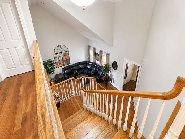 A spacious living area with a black leather sectional sofa, a wooden staircase with white balusters, and a large mirror on the wall.