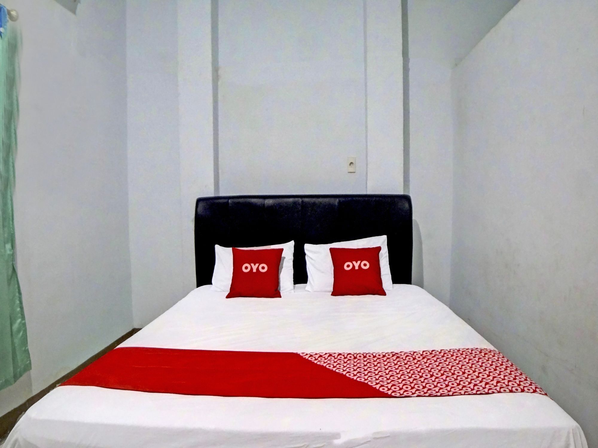 A single bed with a black headboard, two red pillows with 'OYO' text, and a white and red bedspread.