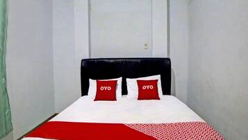 A single bed with a black headboard, two red pillows with 'OYO' text, and a white and red bedspread.