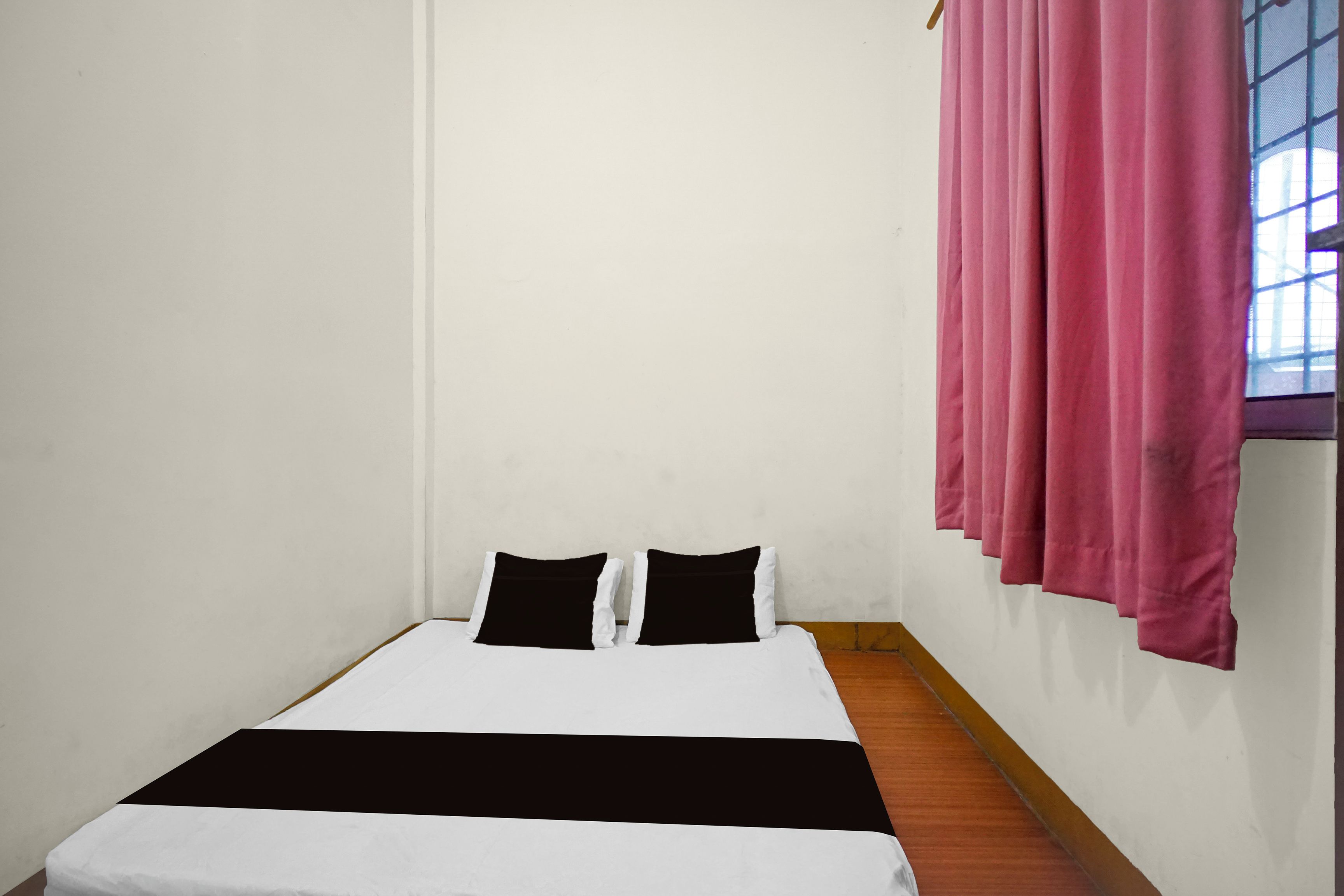 A single bed with a black and white bedspread, two black pillows, and a wooden floor.