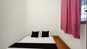 A single bed with a black and white bedspread, two black pillows, and a wooden floor.