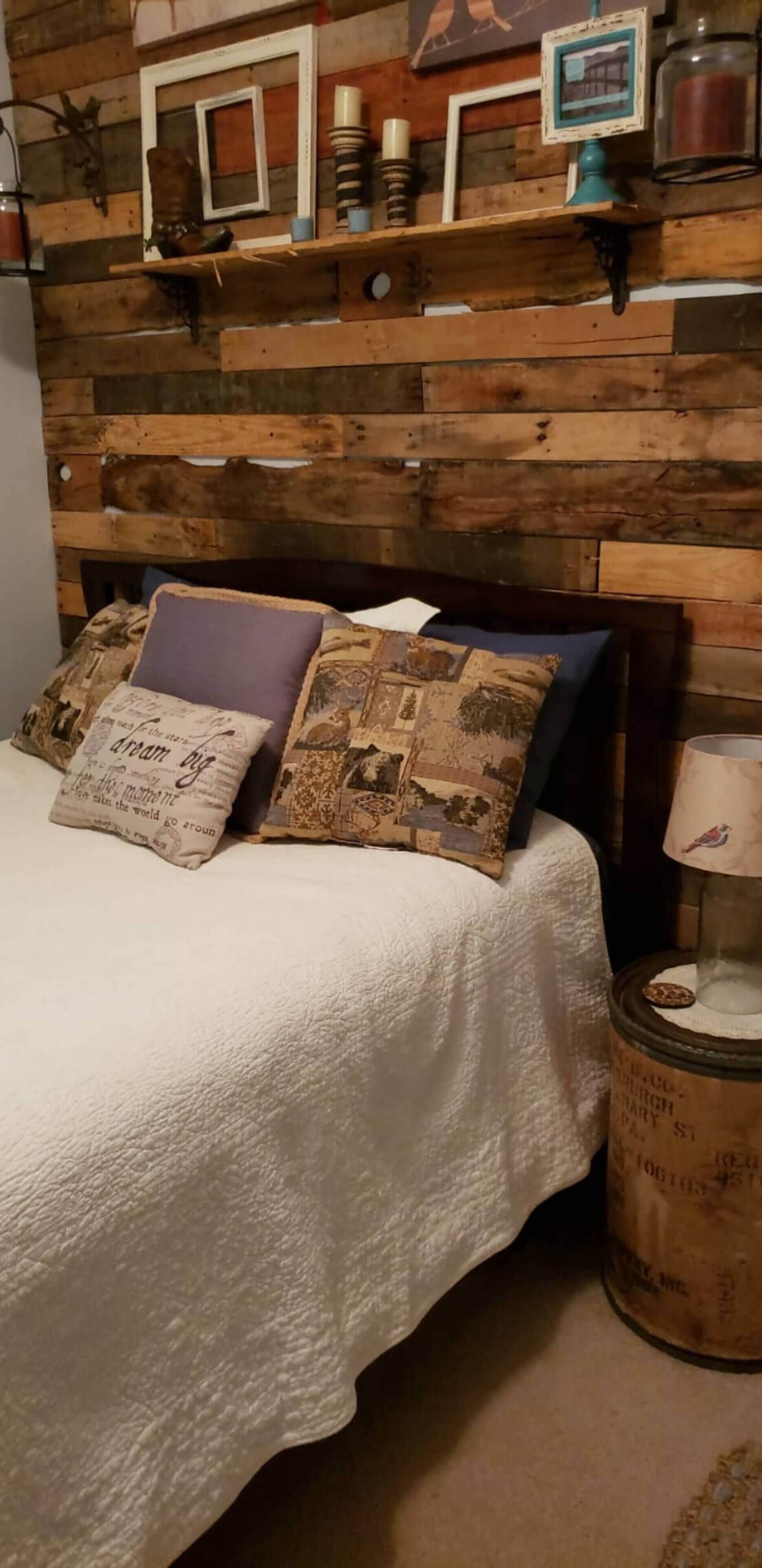 Un letto con copriletto bianco e due cuscini decorativi, una testiera in legno dal finish rustico e un comodino con una lampada.