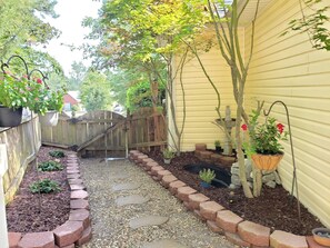 Un chemin de jardin bordé de pierres plates, une clôture en bois et diverses plantes en pot.