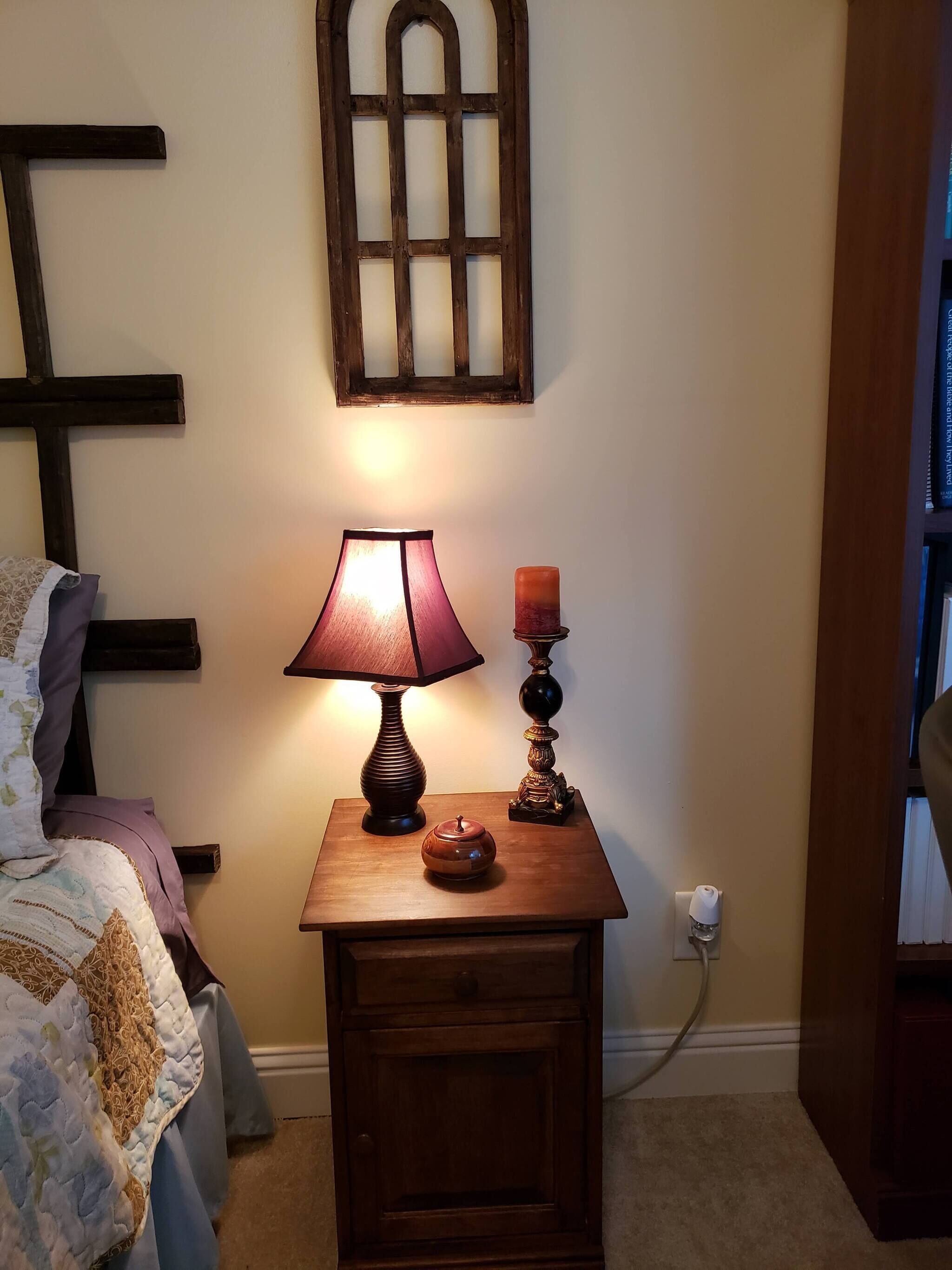 A wooden bedside table with a lamp, a candle, and a small decorative item.