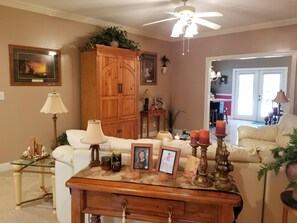 Un salon avec un canapé blanc, un meuble en bois, une table basse en verre et un ventilateur de plafond.