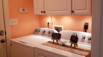 A laundry room with a front-loading washer and dryer, white cabinets above, and a small chalkboard with laundry tips.