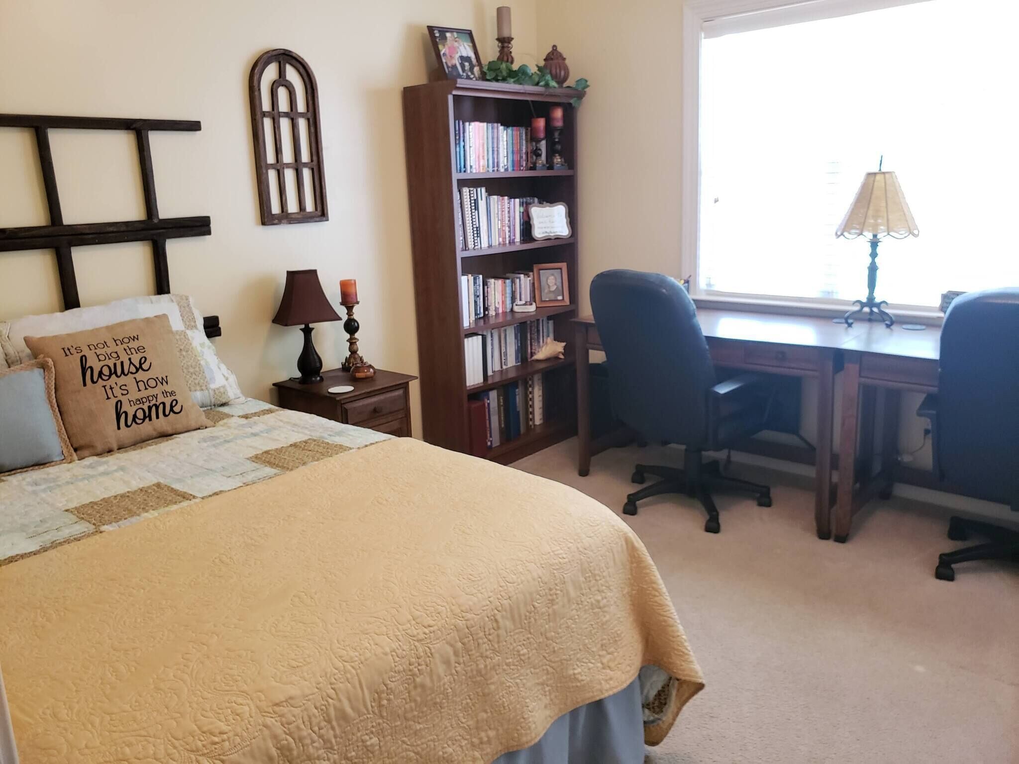 A bedroom with a bed, a bookshelf, a desk, and a window.