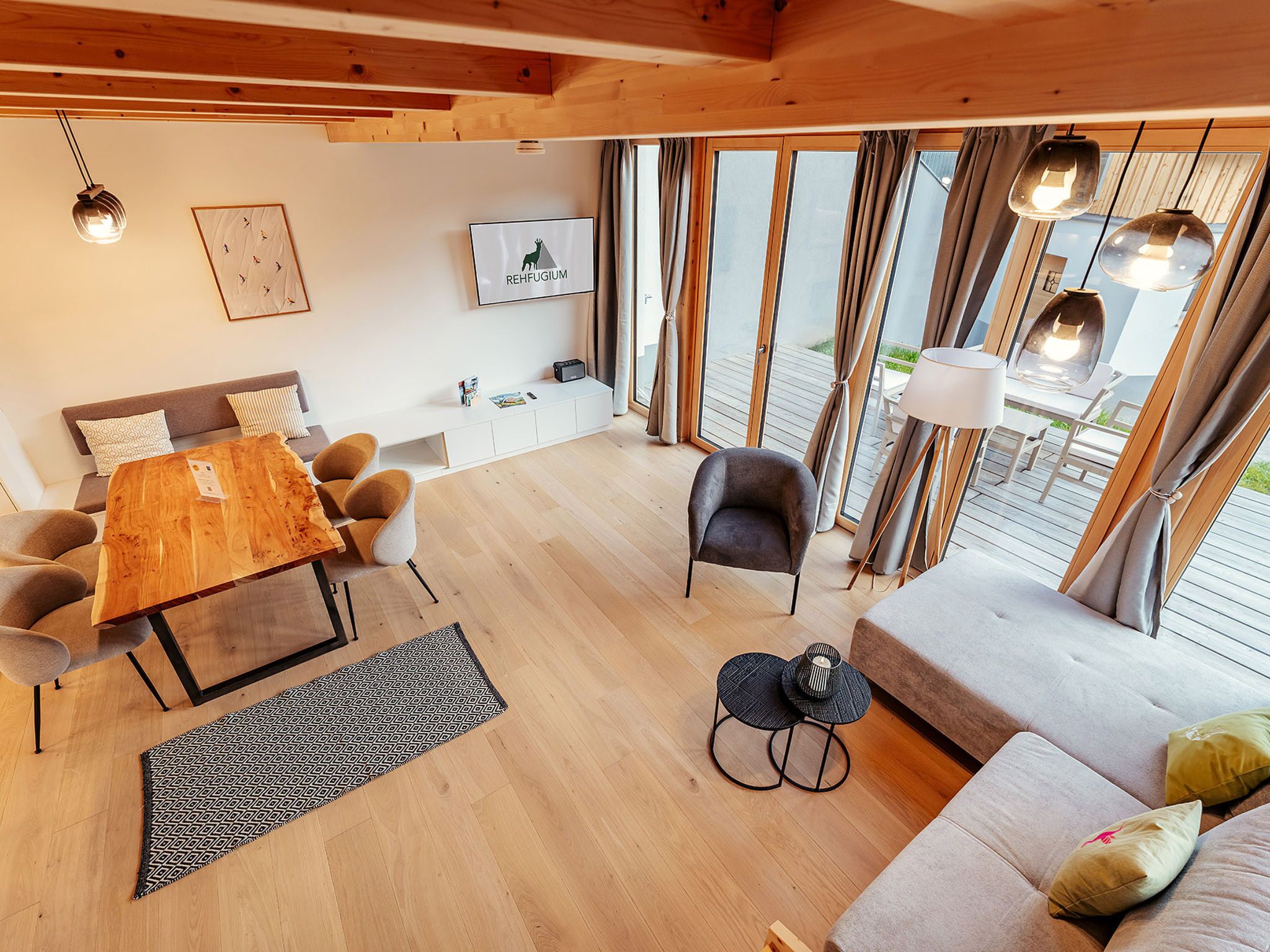 Ein stilvoller Wohnraum mit Esstisch aus Holz, einer Couch, Sesseln, einem kleinen Beistelltisch und einem Fernseher.