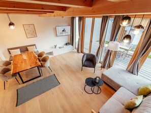 A modern living space with a wooden dining table, sofa, and chairs, a small side table, and a TV. - Chalet Nr. 3 mit 3 SZ, Sauna & Whirlpool by Interhome (Niederwölz)