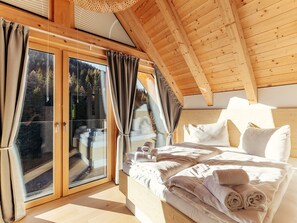 A bedroom with a wooden ceiling, a large bed with white linens, and a sliding glass door leading to an outdoor area. - Chalet Nr. 5 mit 2 Schlafzimmern und Sauna by Interhome (Niederwölz)
