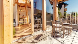 Eine Holzterrasse mit Gartenmöbeln, ein Glastür-Eingang und Blick auf die umliegende Landschaft.