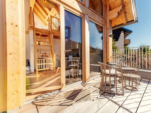 Eine Holzterrasse mit Gartenmöbeln, ein Glastür-Eingang und Blick auf die umliegende Landschaft.