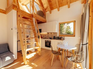 A modern kitchen with wooden beams, a dining area with a table and chairs, and a loft bedroom with a wooden ladder. - Chalet Nr. 6 für 2 Personen mit Sauna by Interhome (Niederwölz)