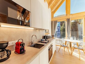A modern kitchen with a built-in stove, sink, and a dining area with a table and chairs. - Chalet Nr. 6 für 2 Personen mit Sauna by Interhome (Niederwölz)